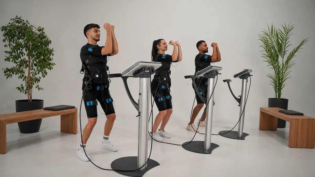 Un groupe de trois peronnes dont une femmme pratiquant du sport via l'électrostimulation en tenue de sport et électrodes