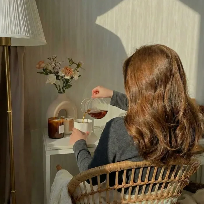 Femme de dos aux cheveux longs auburn assise devant une table avec une tisane à la main